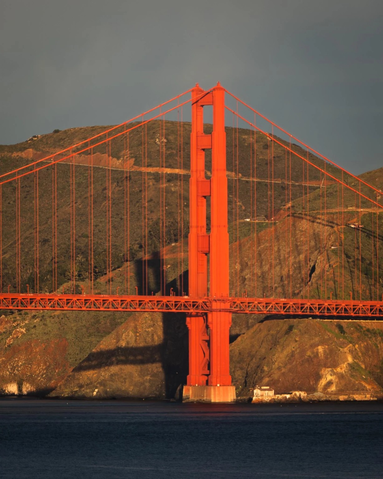 Golden Gate Bridge western tower illuminated against the Marin Headlands